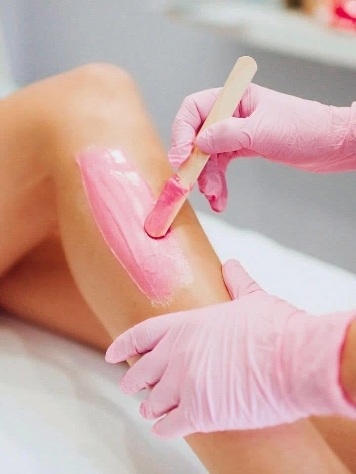Leg waxing with pink wax and gloved hands